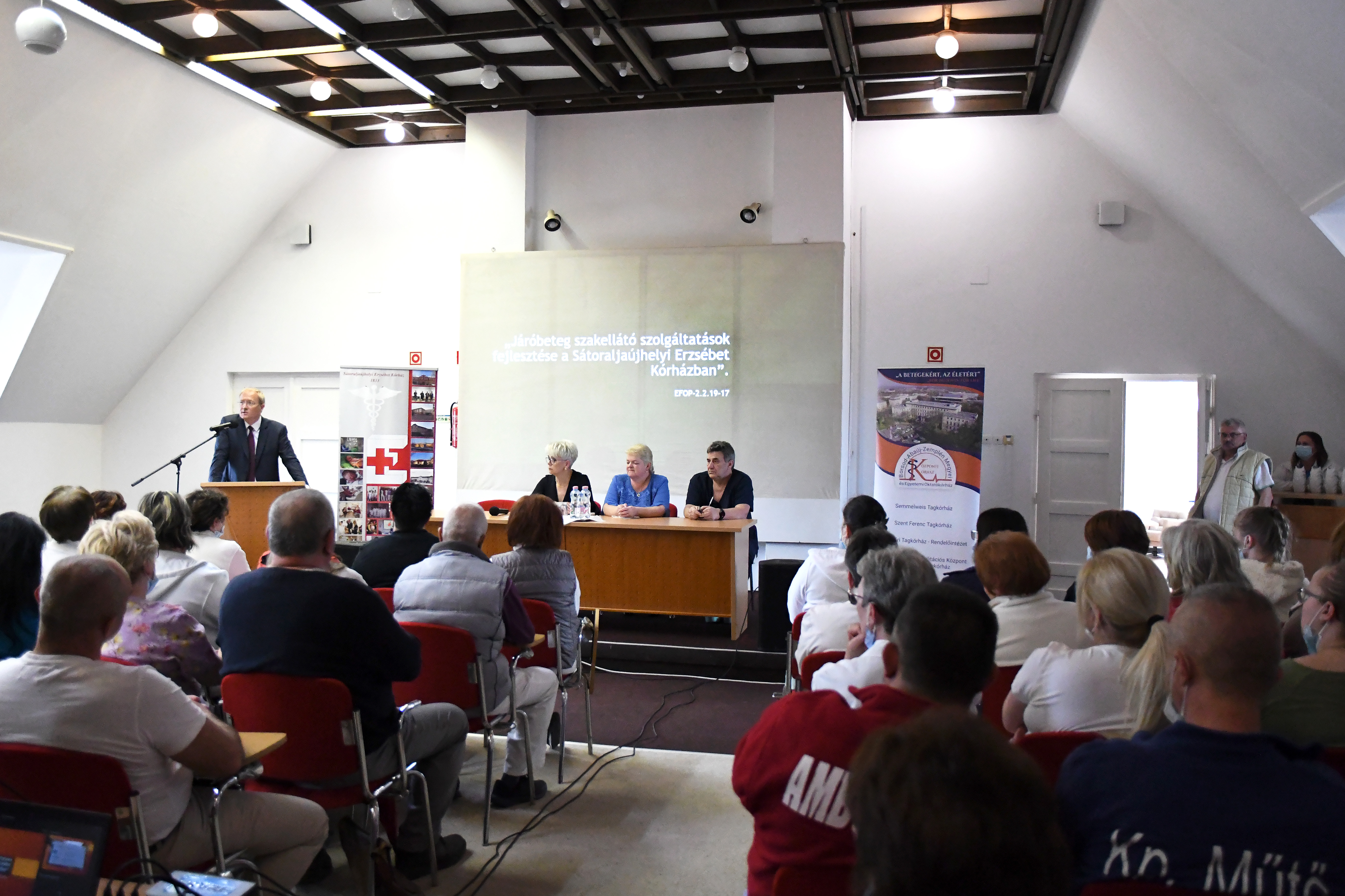 Emberek ülnek egy asztalnál közönség előtt